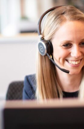 Smilende kvinde fra kundeservice med headset på foran to computerskærme