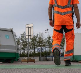 Underkroppen af en mand i orange arbejdstøj med to containere i baggrunden